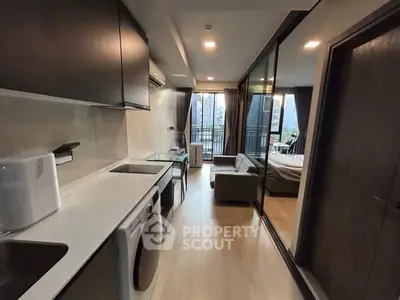 Modern studio apartment with sleek kitchen and cozy living area, featuring a balcony with city view.
