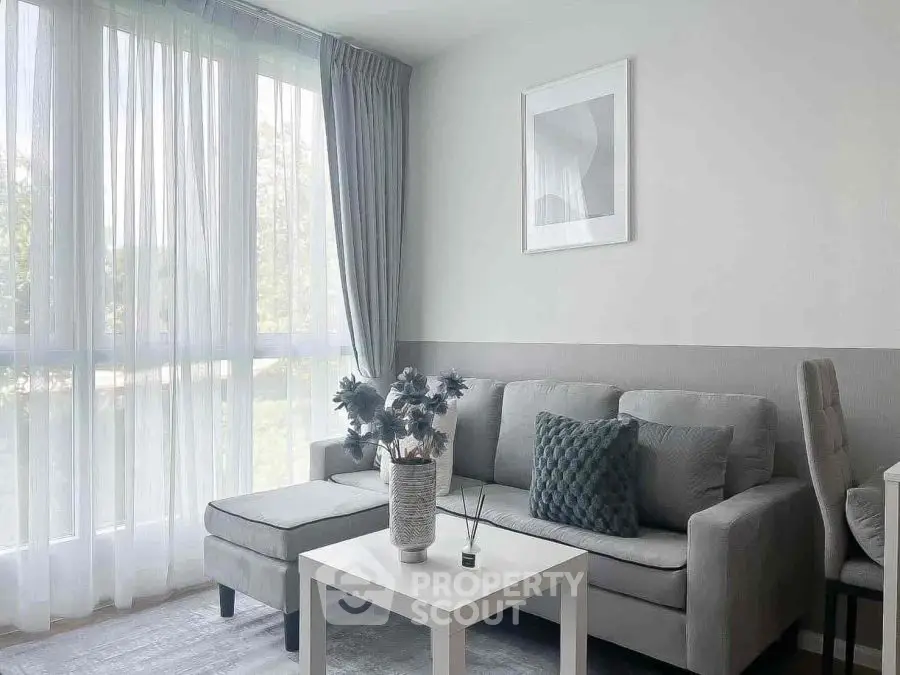 Modern living room with gray sofa, elegant decor, and large window with sheer curtains.