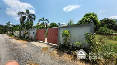 Charming gated entrance to a tropical property with lush greenery and palm trees.