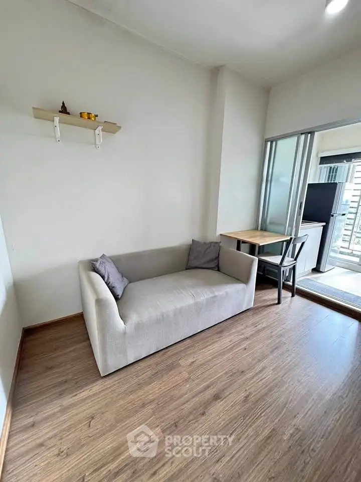Modern living room with sleek sofa and wooden flooring, adjacent to a bright balcony area.