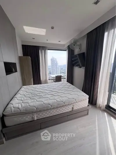 Modern bedroom with city view, featuring a large bed and floor-to-ceiling windows for natural light.