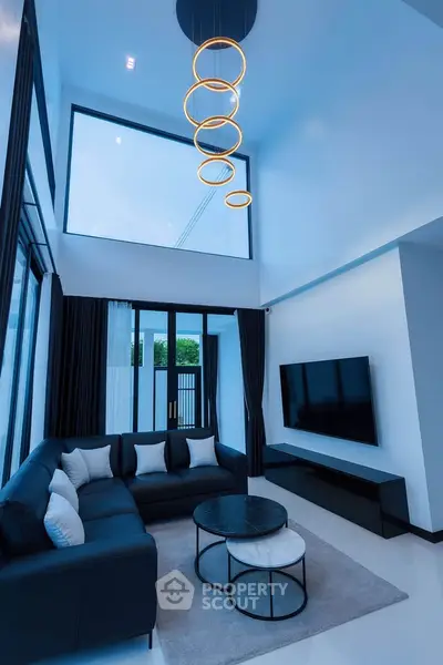 Modern living room with high ceiling, stylish chandelier, and large windows for natural light.