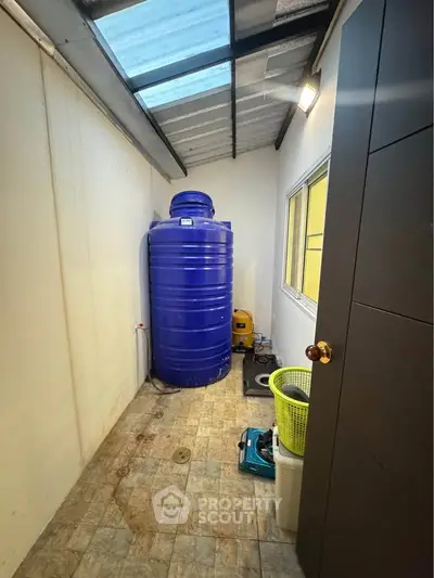 Utility room with large blue water tank and tiled floor, featuring a skylight roof.