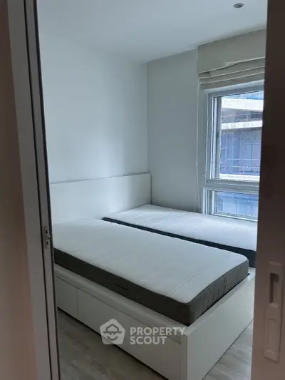 Modern bedroom with twin beds and large window, offering natural light and a minimalist design.