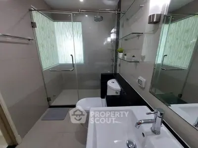 Modern bathroom with glass shower enclosure, sleek fixtures, and natural light filtering through frosted windows, offering a serene and refreshing space.