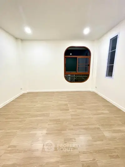 Spacious empty room with elegant wooden flooring and unique arched window design.