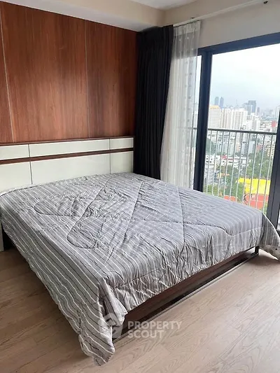 Modern bedroom with city view and large window, featuring a cozy bed and wooden accents.