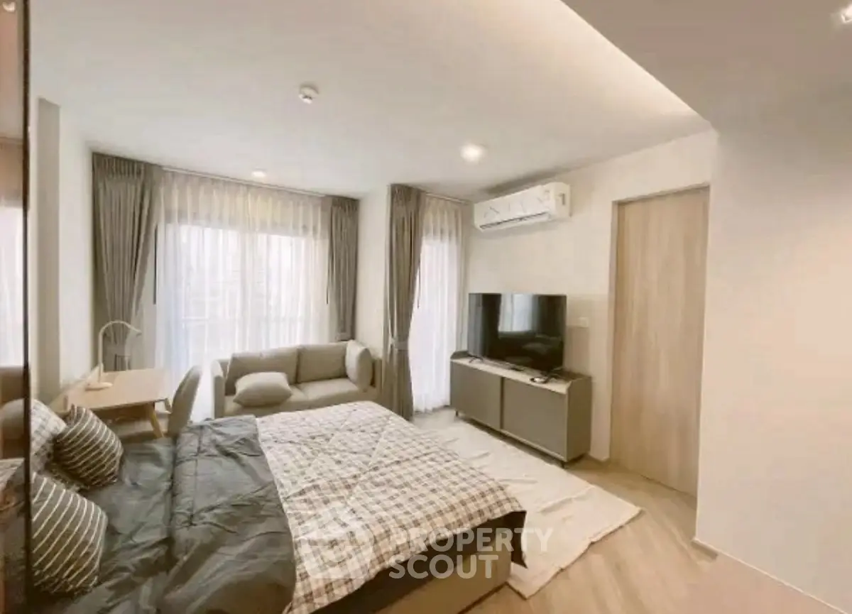 Modern bedroom with cozy sofa and TV, featuring elegant curtains and stylish decor.