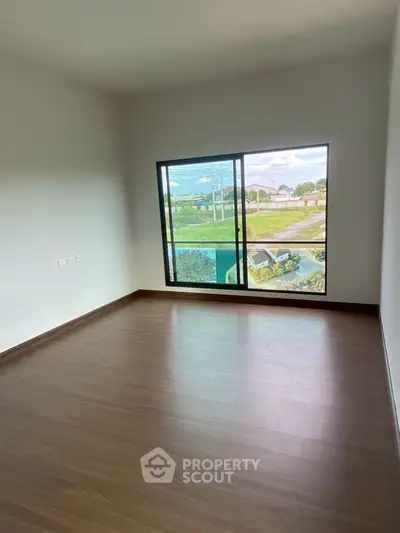 Spacious empty room with large window and wooden flooring
