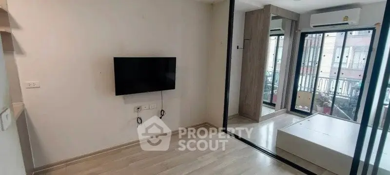Modern living room with wall-mounted TV and large windows offering natural light.