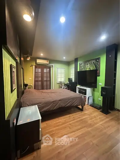 Spacious bedroom with modern decor and wooden flooring, featuring a large bed and entertainment setup.