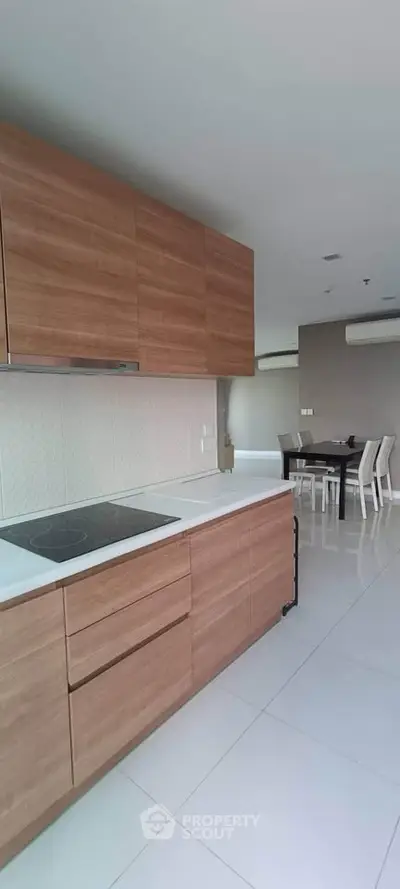 Modern kitchen with sleek wooden cabinets and dining area in open layout apartment.