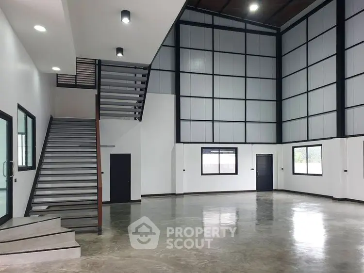 Spacious modern industrial-style interior with high ceilings and large windows.