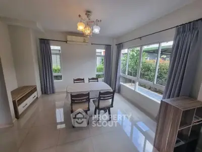 Bright dining area with large windows and garden view, featuring elegant chandelier and modern furniture.