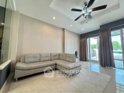 Spacious living room with modern L-shaped sofa and ceiling fan, featuring large windows for natural light.