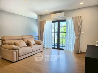 Spacious living room with cozy sofa and large windows leading to a balcony, perfect for relaxation.