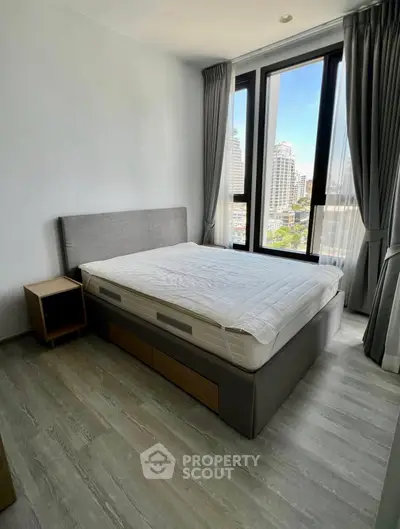 Modern bedroom with large windows and city view, featuring a stylish bed and sleek flooring.