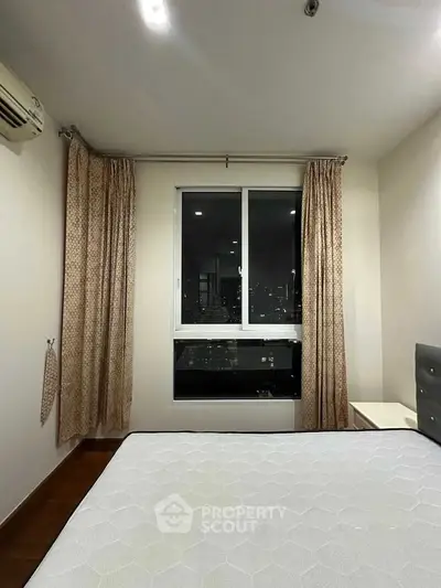 Cozy bedroom with city view, featuring a large window and elegant curtains, perfect for urban living.