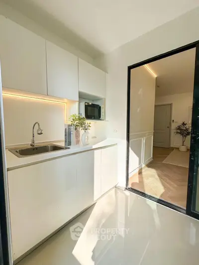 Modern kitchen with sleek white cabinets and natural light, featuring a stylish faucet and decorative plants.