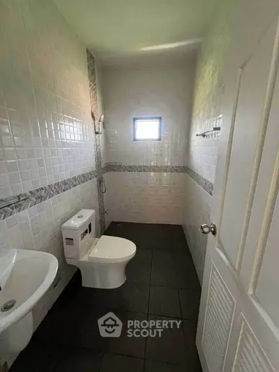 Compact bathroom with modern fixtures and tiled walls, featuring a small window for natural light.