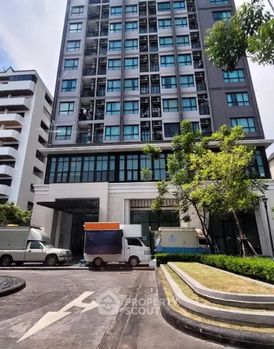 Modern high-rise building exterior with lush landscaping and parked vehicles in front.