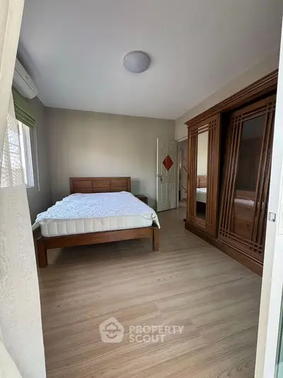 Spacious bedroom with wooden furniture and natural light, perfect for relaxation.