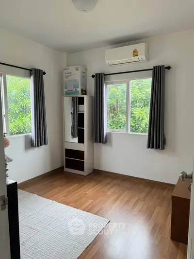 Bright bedroom with wooden flooring and air conditioning, featuring large windows with garden view.