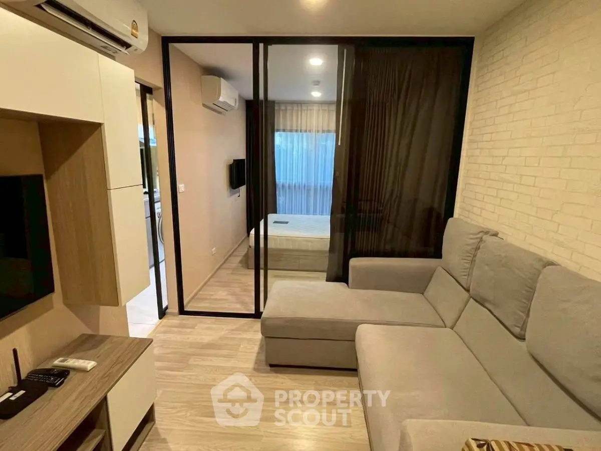 Modern living room with cozy gray sofa and glass partition leading to bedroom