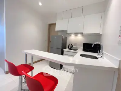 Modern kitchen with sleek white cabinets and red bar stools, featuring stainless steel appliances.