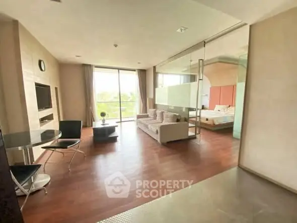 Spacious modern living room with wooden flooring and glass partition leading to bedroom.