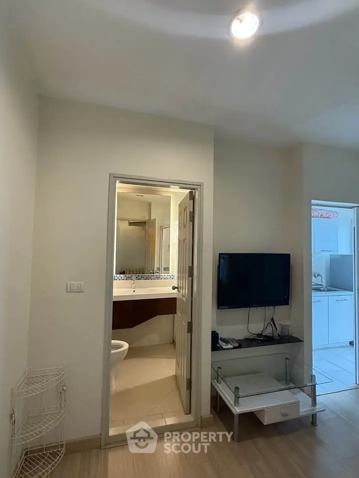 Modern apartment interior with bathroom and living area featuring TV and glass table.