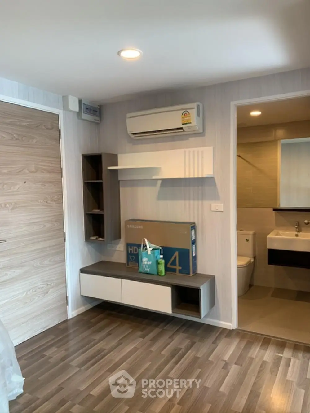 Modern apartment interior with wooden flooring, wall-mounted shelves, and air conditioning unit.