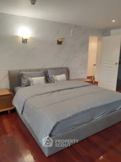 Spacious bedroom with elegant decor and hardwood flooring, featuring a comfortable bed and stylish lighting.