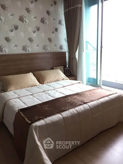 Elegant bedroom with floral wallpaper and large window offering natural light.