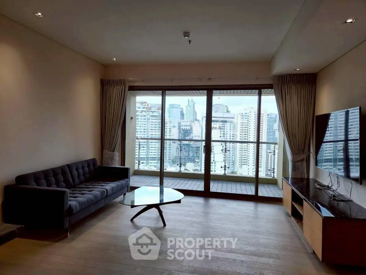 Spacious living room with modern furniture and city view balcony in high-rise apartment.