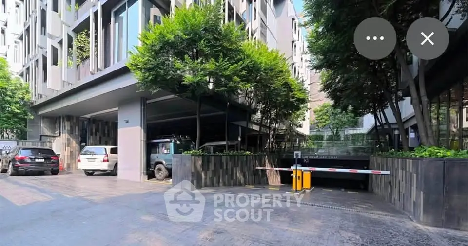 Modern apartment building entrance with lush greenery and secure parking access.
