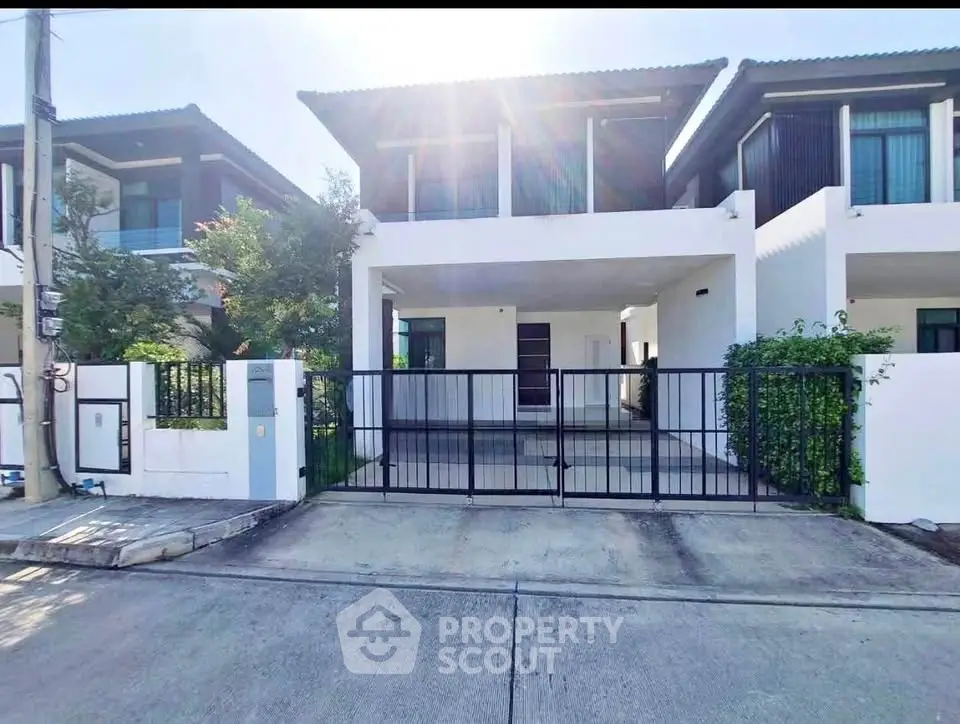 Modern two-story house with gated driveway and lush greenery in a serene neighborhood.