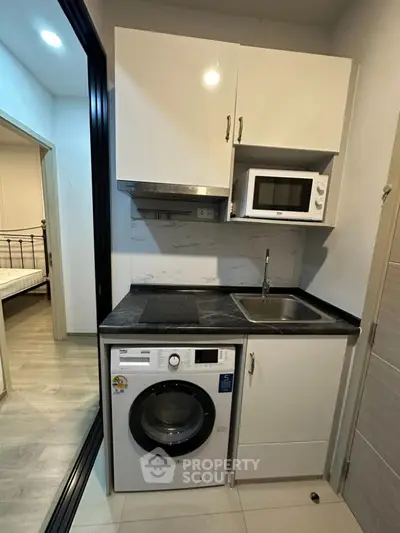Compact kitchen with modern appliances including washing machine and microwave, adjacent to bedroom.