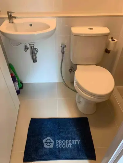 Compact bathroom with white fixtures and blue mat, ideal for small spaces.