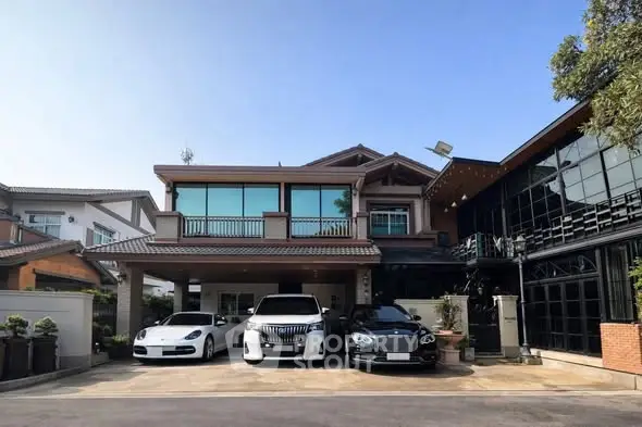 Luxurious modern house with spacious driveway and three luxury cars parked in front, showcasing elegant architecture.