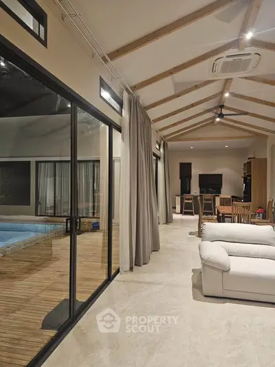 Luxurious open-plan living room with pool view and modern wooden ceiling beams.