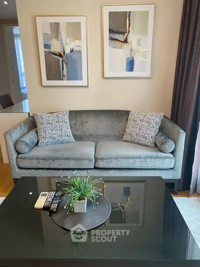 Stylish living room with modern gray sofa, abstract art, and sleek glass coffee table.