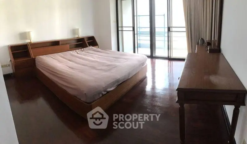 Spacious bedroom with wooden flooring and large windows leading to a balcony.