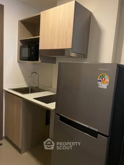 Modern compact kitchen with sleek cabinetry and stainless steel fridge in a stylish apartment.
