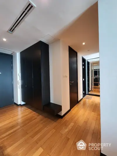 Modern apartment hallway with wooden flooring and sleek black cabinetry