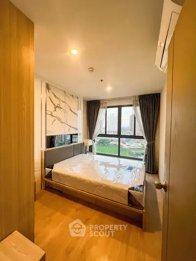 Modern bedroom with large window offering city view, featuring wooden flooring and stylish decor.