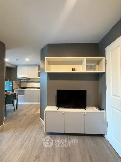 Modern living room with sleek TV unit and open kitchen layout, featuring stylish flooring and contemporary design.