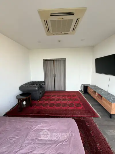 Spacious living room with modern decor, featuring a stylish sofa, wall-mounted TV, and elegant carpet.