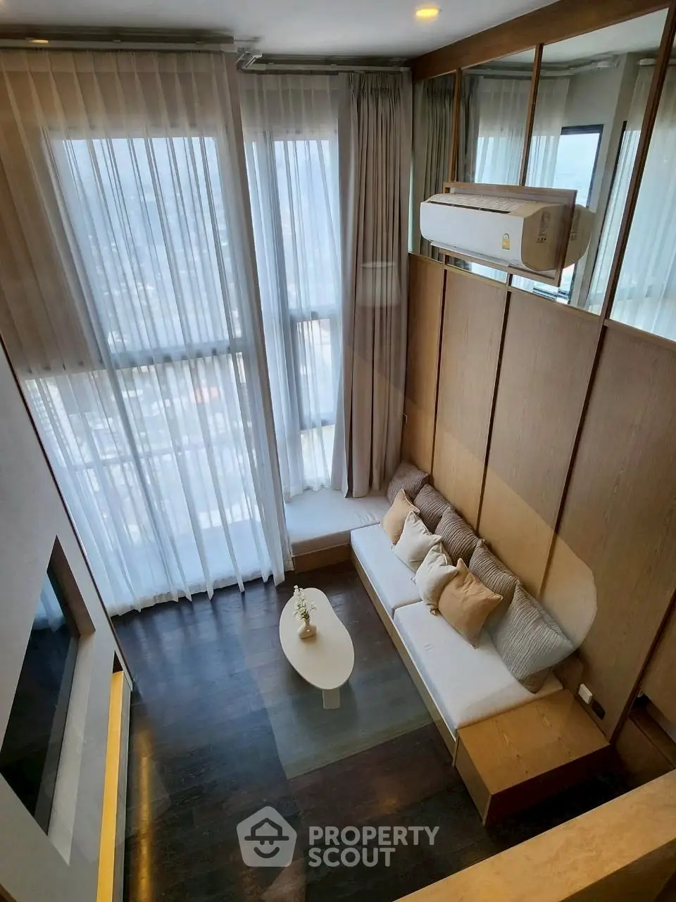 Modern living room with high ceilings and large windows offering city views.