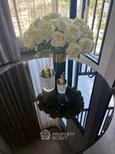Elegant interior with a round glass table and white roses, offering a stunning city view through large windows.